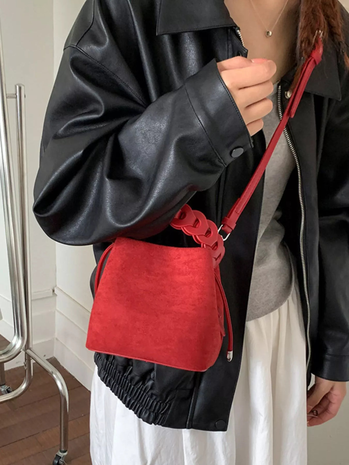 Red crossbody bag with a chain detail on the strap, worn over a black leather jacket