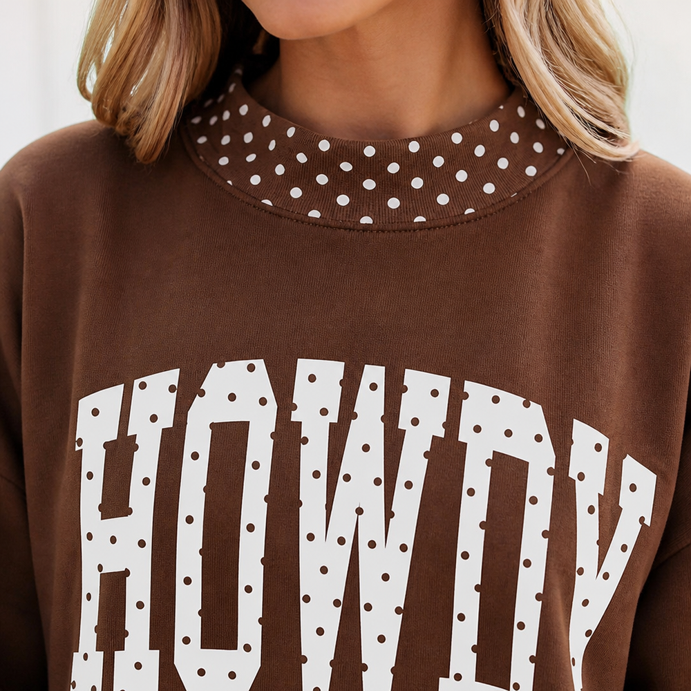 Close-up of a person wearing a brown sweatshirt with a white polka-dot patterned collar and large white arched text reading 'HOWDY' across the front.